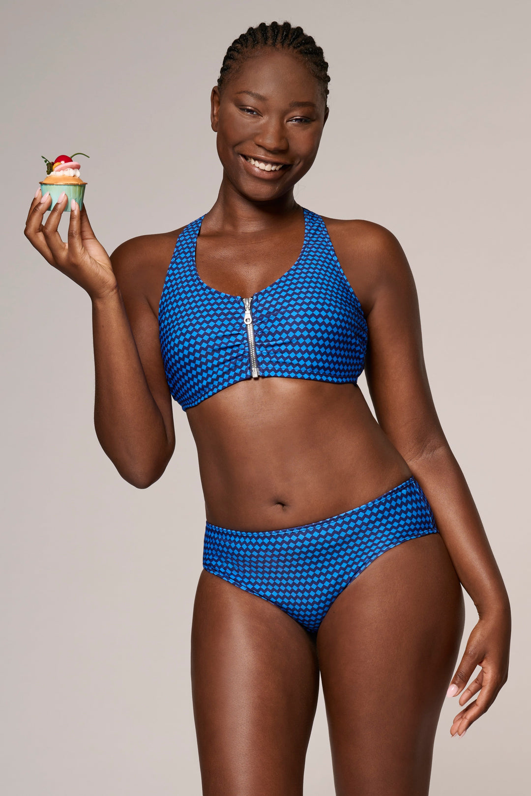 Woman in a blue bikini holding a cupcake against a plain background